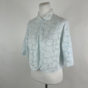 May include: A light blue lace top with a button-up front and short sleeves. The top has a delicate floral pattern and a rounded hem.