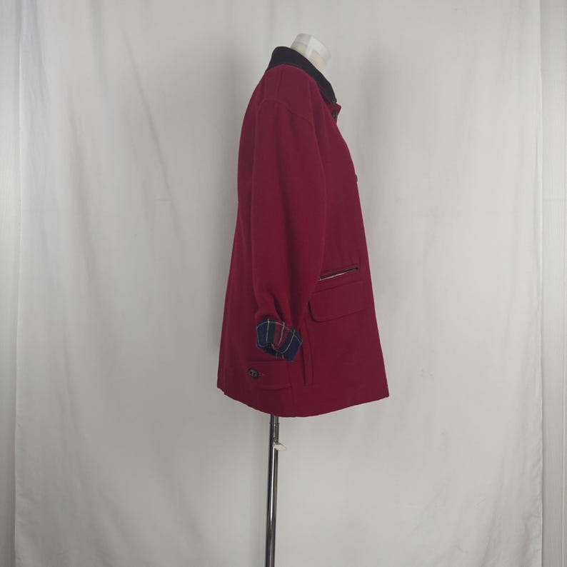 Op de afbeelding: Een bordeauxrode jas met een zwarte kraag en geruite manchetten. De jas heeft twee voorzakken en een ritssluiting op de borst. De jas wordt op een mannequin getoond.