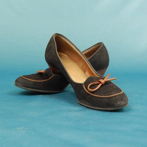 May include: A pair of black suede heeled shoes with brown leather trim and a bow detail.