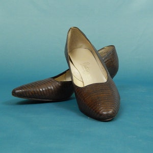 May include: A pair of brown leather pumps with a pointed toe and a low heel. The shoes have a textured, snake-like pattern.
