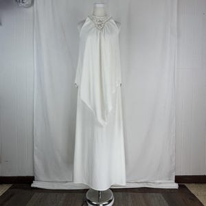 May include: A white halter-neck dress with a flowing, layered design. The dress features a detailed, beaded neckline and a floor-length skirt. The fabric appears to be a soft, lightweight material, suitable for formal occasions.