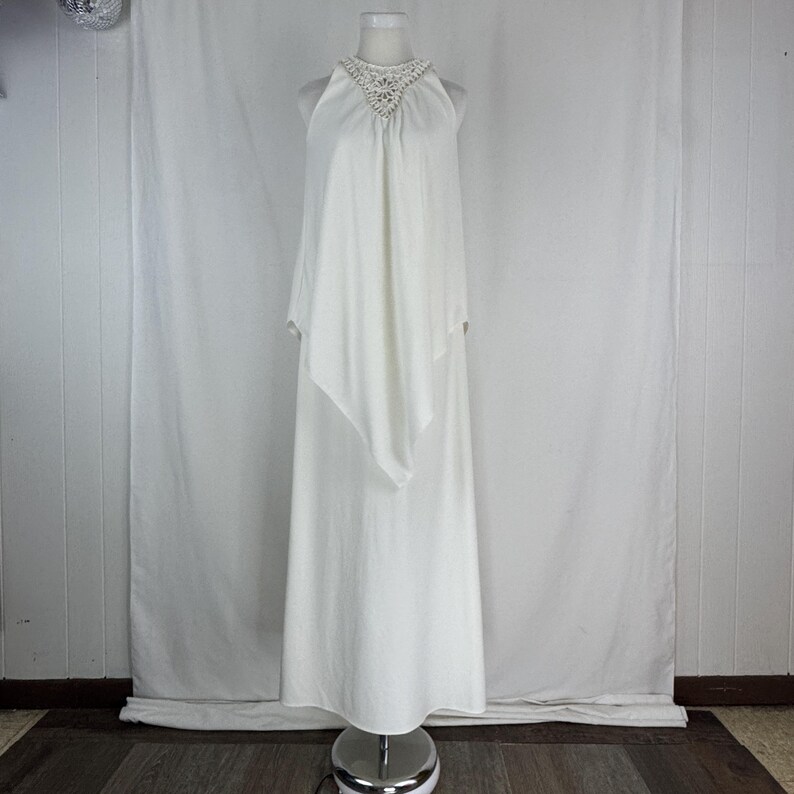 May include: A white halter-neck dress with a flowing, layered design. The dress features a detailed, beaded neckline and a floor-length skirt. The fabric appears to be a soft, lightweight material, suitable for formal occasions.
