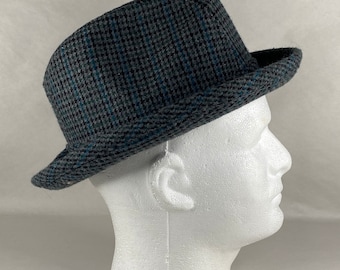 May include: A gray and blue patterned fedora hat with a wide brim. The hat is made of a soft, textured fabric.