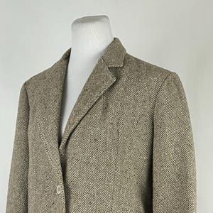 Puede incluir: Una chaqueta de punto marrón y beige con diseño de espiga y cierre de un botón.