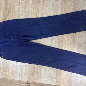 May include: Dark blue denim pants with a classic five-pocket design. The pants have a straight leg cut and a small embroidered horse logo on the front pocket. The pants are laid flat on a wooden surface.