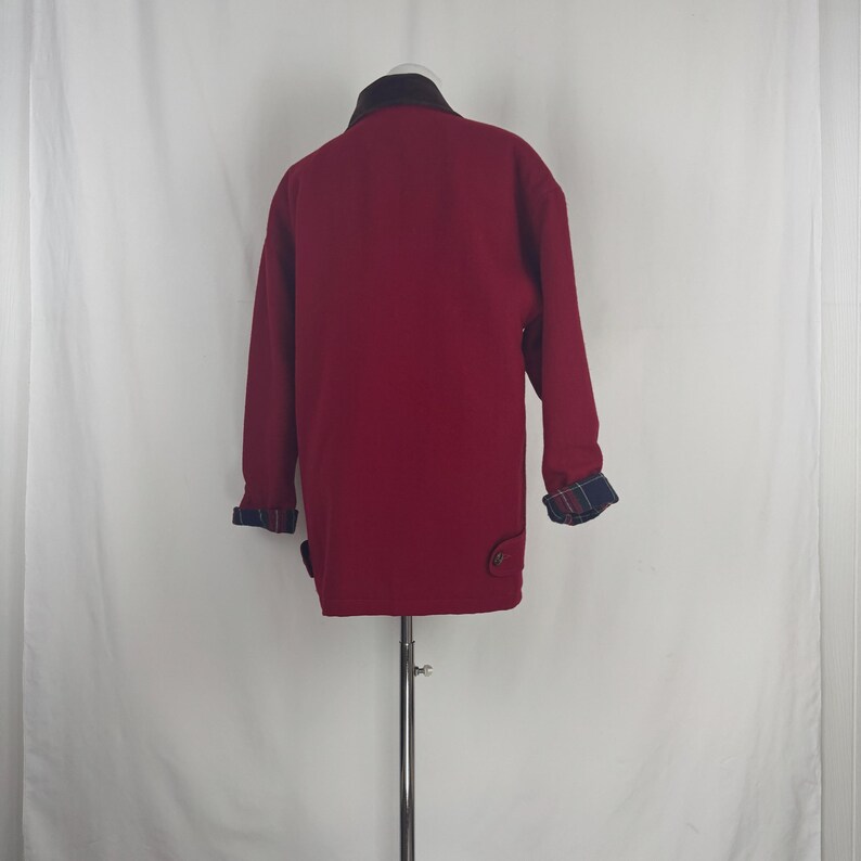 Op de afbeelding: Bordeaux jas met een donkerbruine kraag en geruite manchetten. De jas heeft twee knopen aan de voorkant en een klassiek ontwerp. De mouwen zijn lang en de jas wordt op een mannequin gepresenteerd.