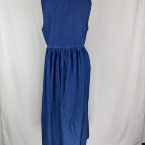 May include: A sleeveless, blue denim dress with a V-neckline and a gathered waist. The dress has a midi length and is displayed on a mannequin. The denim fabric has a classic, medium wash.