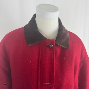 May include: A red wool coat with a brown suede collar and button closure. The coat is displayed on a white mannequin. The coat has a classic design, suitable for cold weather. The coat has a button closure and a brown suede collar.