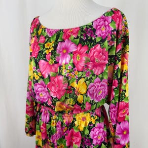 Puede incluir: Un vestido negro de manga larga con estampado floral de flores rosas, amarillas y verdes. El vestido tiene una cintura fruncida y un escote ligeramente caído.