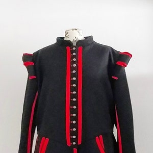 May include: A black doublet with red trim and accents, featuring a high collar and decorative buttons down the front. The sleeves have shoulder puffs, and the garment is displayed on a mannequin.