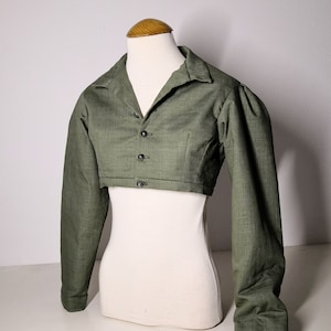 May include: A green cropped jacket with a collar and button fastening. The jacket has long sleeves and a fitted silhouette.