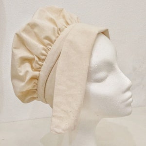 May include: A white linen bonnet with a gathered crown and a long, flowing flap that can be tied under the chin.