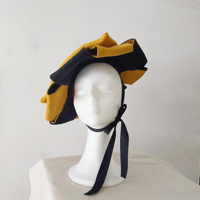Puede incluir: Un sombrero de tela amarillo y negro con un dise&ntilde;o de volantes y una cinta negra.