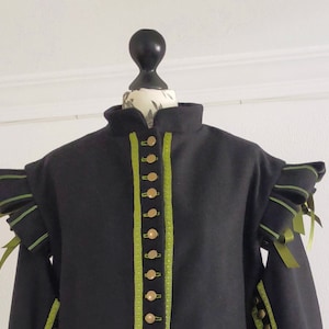 May include: A black jacket with green trim and gold buttons. The jacket has a high collar and ruffled sleeves.