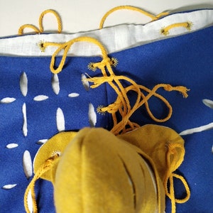 May include: A pair of blue pants with white cutouts and yellow laces. The pants are tied at the waist with a yellow cord.