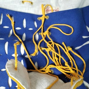 May include: A blue fabric bag with a yellow drawstring and white fabric lining. The bag has a cut-out design and is tied with a yellow cord.