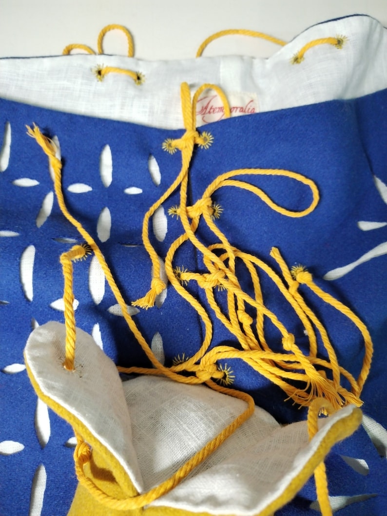 May include: A blue fabric bag with a yellow drawstring and white fabric lining. The bag has a cut-out design and is tied with a yellow cord.
