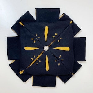 May include: A black fabric starburst with yellow cutouts and a silver button in the center.