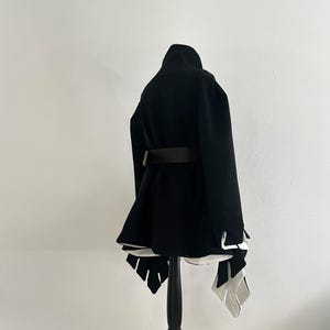 May include: A black coat with a high collar and a brown belt. The coat has a flared skirt and white accents at the hem. It is displayed on a black mannequin.