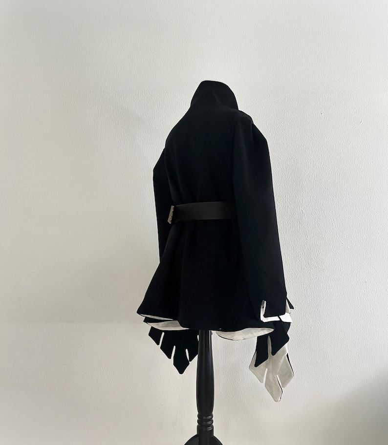 May include: A black coat with a high collar and a brown belt. The coat has a flared skirt and white accents at the hem. It is displayed on a black mannequin.