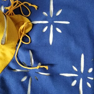 May include: A blue fabric banner with three white star-shaped cutouts. The banner has a yellow fabric border and yellow string ties.
