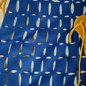 May include: A blue fabric bag with a white background and a pattern of oval cutouts. The bag has a yellow drawstring.