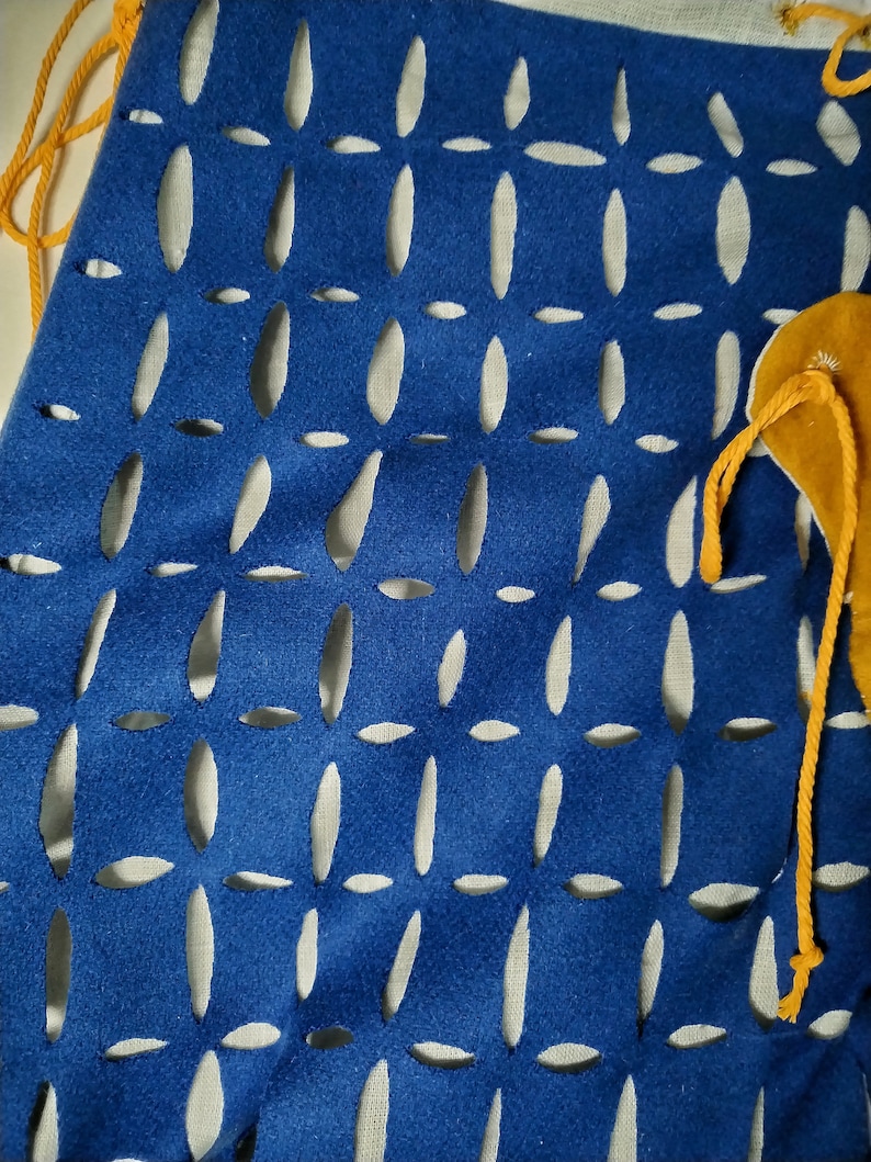 May include: A blue fabric bag with a white background and a pattern of oval cutouts. The bag has a yellow drawstring.