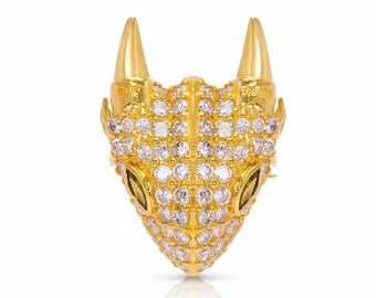 Puede incluir: Un dije de cabeza de dragón dorado con brillantes transparentes y verdes. El dije está detallado con una superficie texturizada y tiene un hocico puntiagudo.