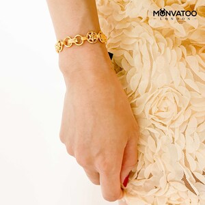 The Golden Constellar Bracelet is worn on a woman's wrist. The women is wearing a cream flower outfit.