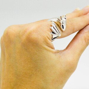 May include: A silver dragon ring with wings wrapped around the finger. The dragon's head is facing forward with its mouth closed.