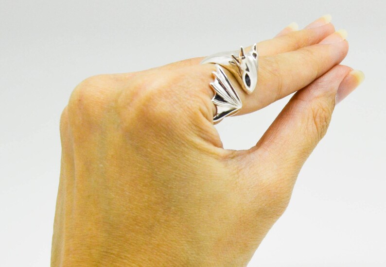 May include: A silver dragon ring with wings wrapped around the finger. The dragon's head is facing forward with its mouth closed.