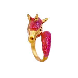 May include: A gold ring with a pink unicorn head design. The unicorn's horn is gold and the head is covered in pink glitter.