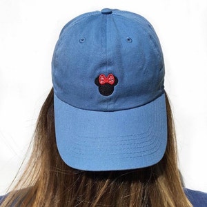 May include: A blue baseball cap with a black and red embroidered Minnie Mouse design.