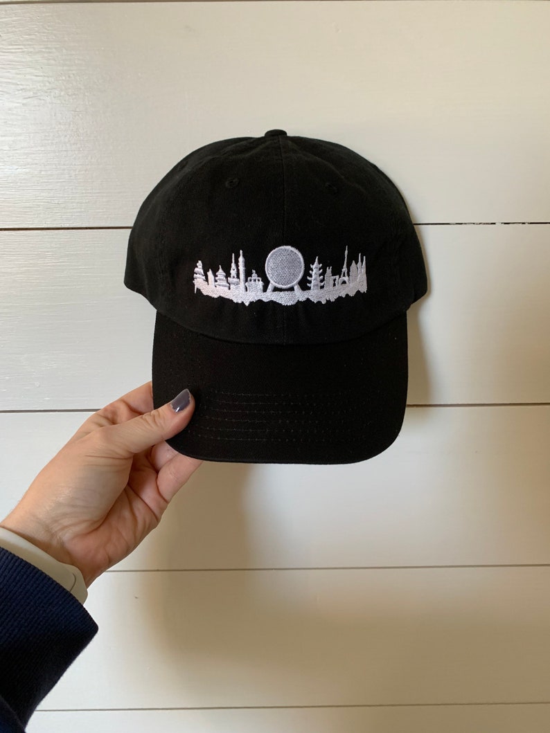 K&ouml;nnte beinhalten: Schwarze Baseballkappe mit einem wei&szlig;en gestickten Design einer Stadtlandschaft mit einem Riesenrad.