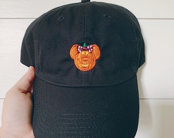 May include: Black baseball cap with an embroidered pumpkin-shaped Mickey Mouse head with a red bow.