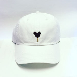 Könnte beinhalten: Weiße Baseballkappe mit einem aufgestickten schwarzen Mickey Mouse-Eis am Vorderteil.