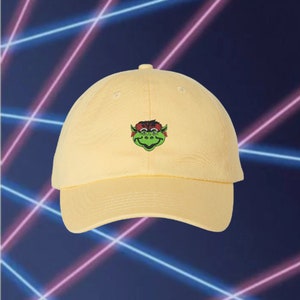 May include: A yellow baseball cap with a green and red cartoon monster embroidered on the front.