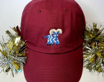 May include: A maroon baseball cap with an embroidered blue and white ram on the front.
