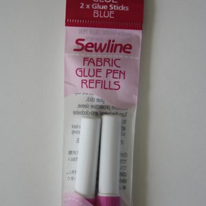 Könnte beinhalten: Eine Packung mit zwei blauen Sewline Fabric Glue Pen Nachfüllpatronen. Die Verpackung ist rosa und weiß mit dem Text "Sewline Fabric Glue Pen Refills" und "GLUE 2 x Glue Sticks BLUE".