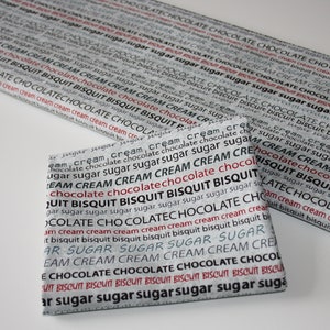 May include: Two fabric squares with a repeating pattern of the words "chocolate", "biscuit", "cream", and "sugar" in black and red text on a white background.