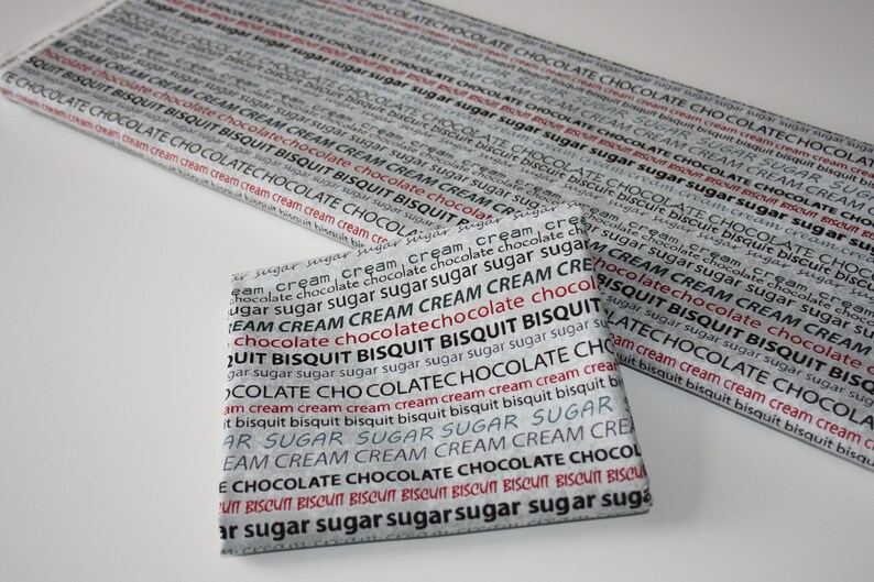 May include: Two fabric squares with a repeating pattern of the words "chocolate", "biscuit", "cream", and "sugar" in black and red text on a white background.
