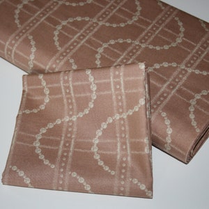 May include: A brown fabric with a white pearl-like chain pattern. The fabric is folded in half, with one side folded over the other.
