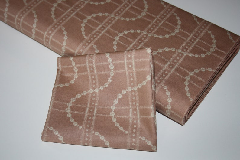 May include: A brown fabric with a white pearl-like chain pattern. The fabric is folded in half, with one side folded over the other.