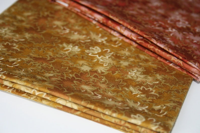 Pu&ograve; includere: Un mucchio di tessuto con un motivo floreale marrone e oro. Il tessuto &egrave; piegato in tre parti e ha una consistenza morbida e testurizzata.