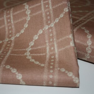 May include: A close-up of a brown fabric with a white pattern of a chain of beads. The fabric has a subtle texture.