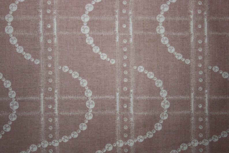 May include: A close-up of a pink fabric with a white pattern of repeating circles and lines. The fabric has a textured surface.