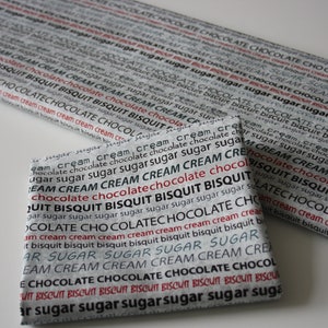 May include: Two pieces of fabric with a repeating pattern of the words "chocolate", "cream", "biscuit", and "sugar" in black and red text on a gray background.