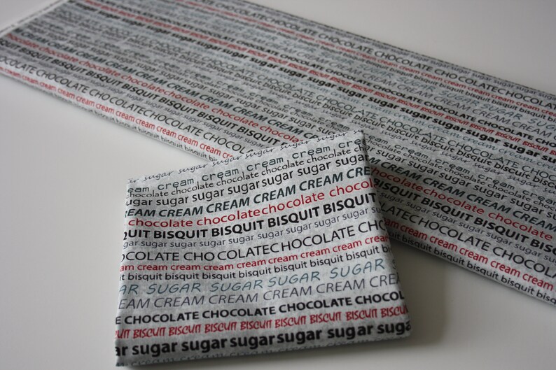 May include: Two pieces of fabric with a repeating pattern of the words "chocolate", "cream", "biscuit", and "sugar" in black and red text on a gray background.