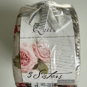 Peut inclure: Un paquet de tissu enveloppé dans du plastique transparent. Le tissu présente un motif floral avec des roses roses et des feuilles vertes. L'étiquette indique "3 Sisters" et comprend une citation d'Helen Keller. Un ruban à mesurer est attaché.