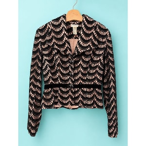 May include: Black lace jacket with a scalloped design, featuring a black velvet belt and button closure. The jacket is hanging on a wooden hanger against a light blue background. The jacket's interior is a light pink color.